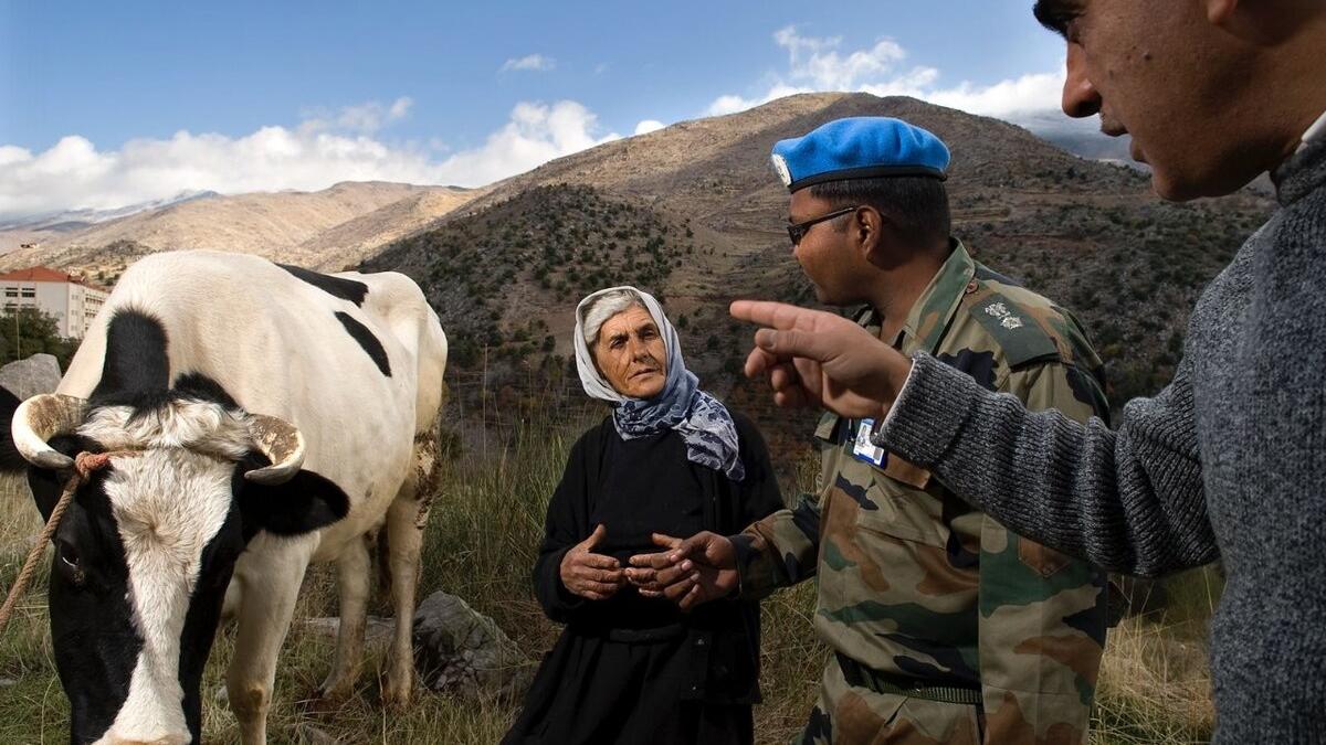 A peacekeeper speaks with two individuals on rural land beside a cow.