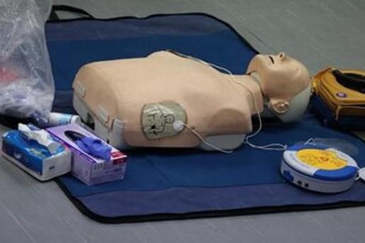 A resuscitation doll on the floor with other medical equipment including a defibrillator